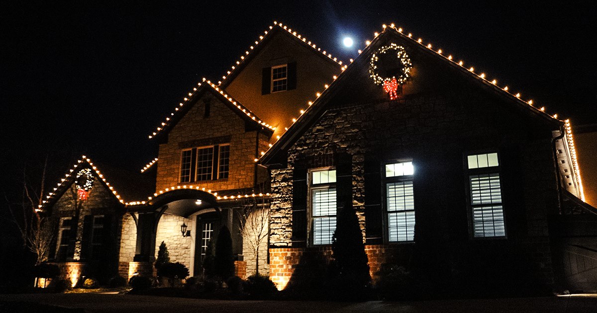 St. Louis stone home at night with warm Christmas lights along the rooflines